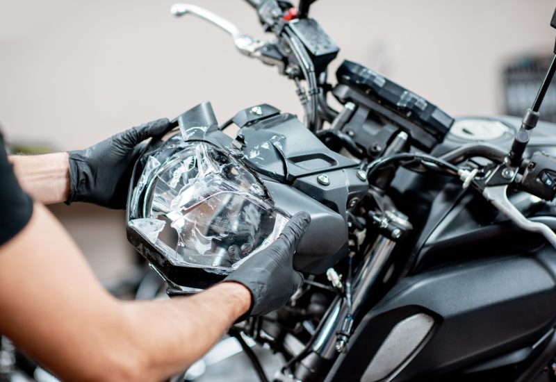 Worker removing broken headlight after the accident, repairing motocycle in the workshop, close-up view